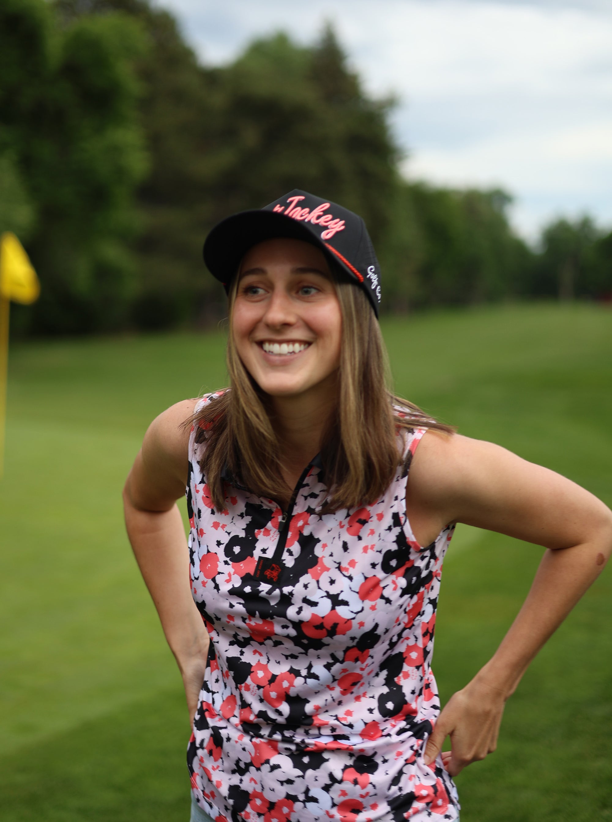 a young woman in a floral top and hat standing on a golf course.